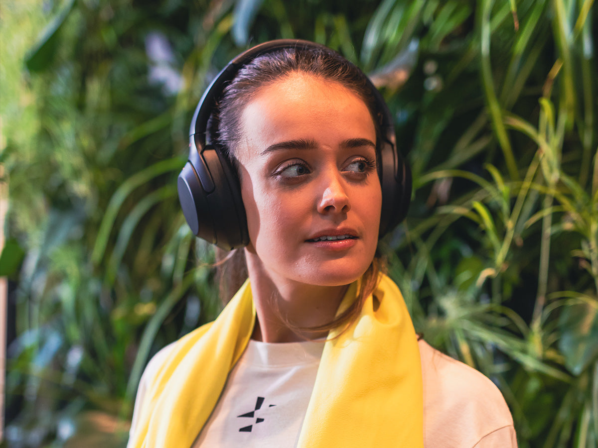 Een model die duurzame sportkleding draagt en voor een wand met groene planten poseert